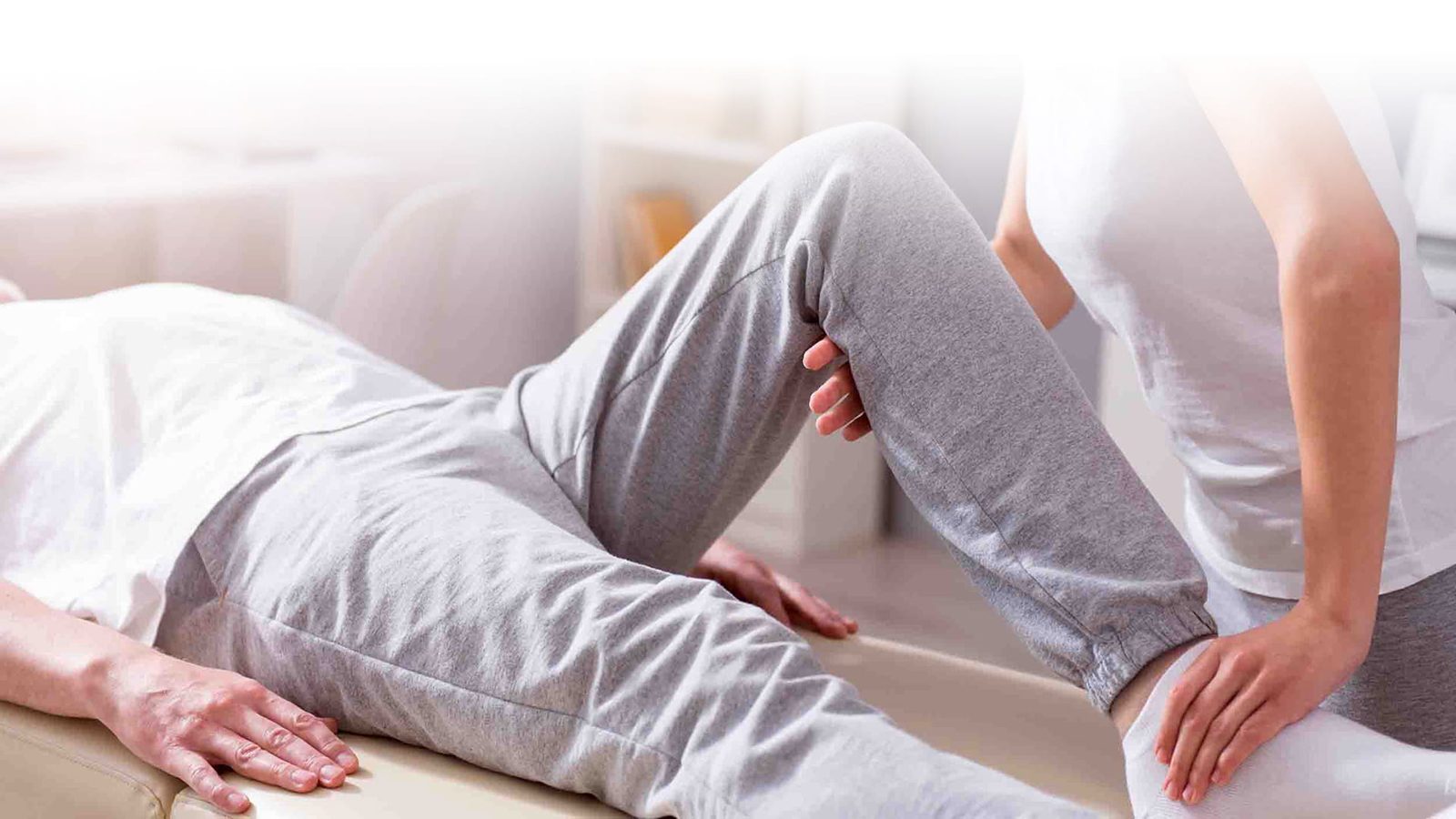 Physiotherapeutin behandelt das Knie einer liegenden Patientin